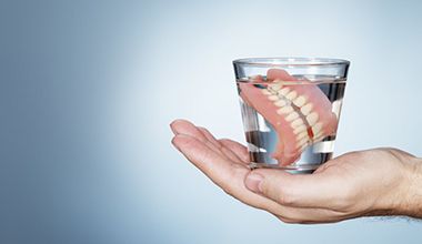 hand holding full dentures in glass of water 