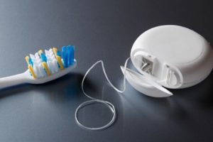 A container of dental floss and a toothbrush laying on a black table